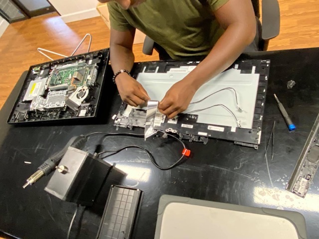 A TechEd and Solutions technician stripping down a laptop at the workbench, with the screen assembly and internals laid out